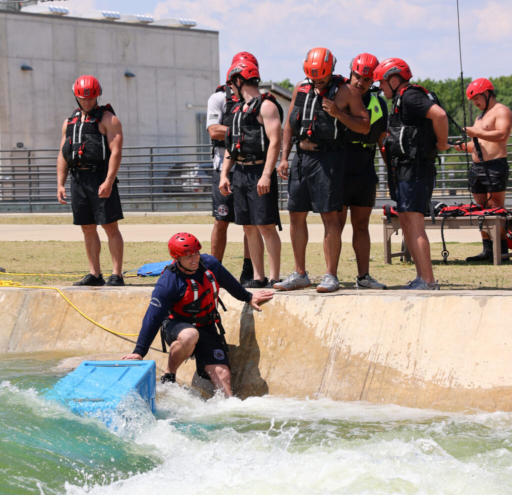 First responder wearing safety gear is entering a man-made water system that has created rapids.
