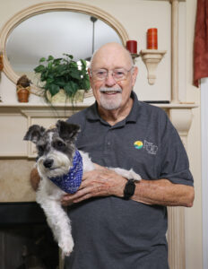 Older man wearing a Mid-South RC&D shirt holding pet dog with smile on his face.